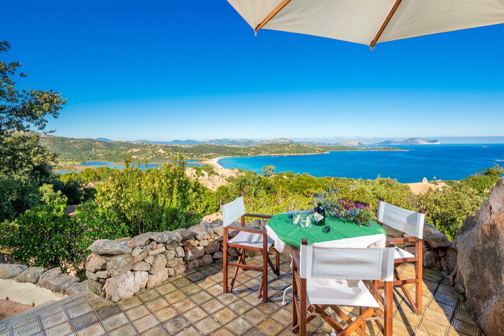 An outdoor table set under an umbrella above the Sardinian coast